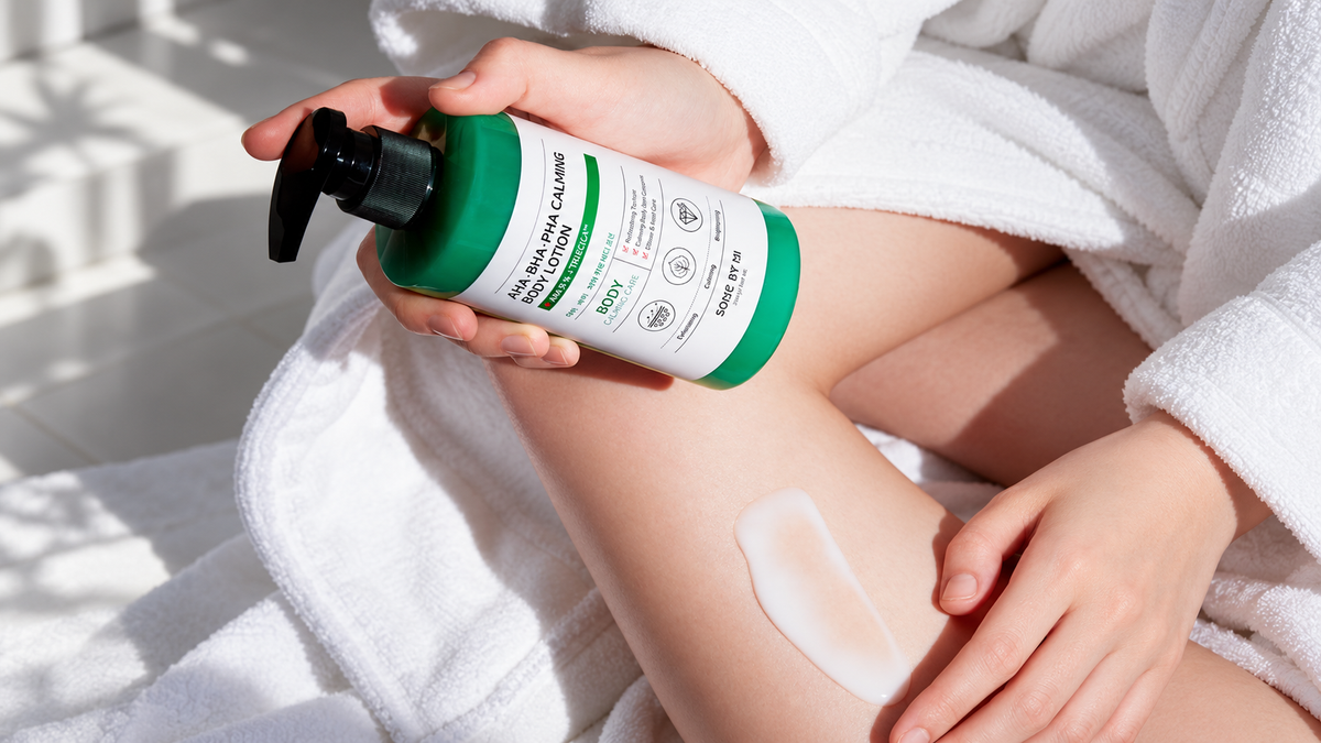 Close-up of hands holding a green-and-white body lotion pump above a leg with a fresh lotion swatch after a shower.