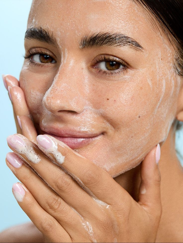 Woman gently removing summer makeup during a double-cleansing routine after wearing sunscreen and spending time in the heat.