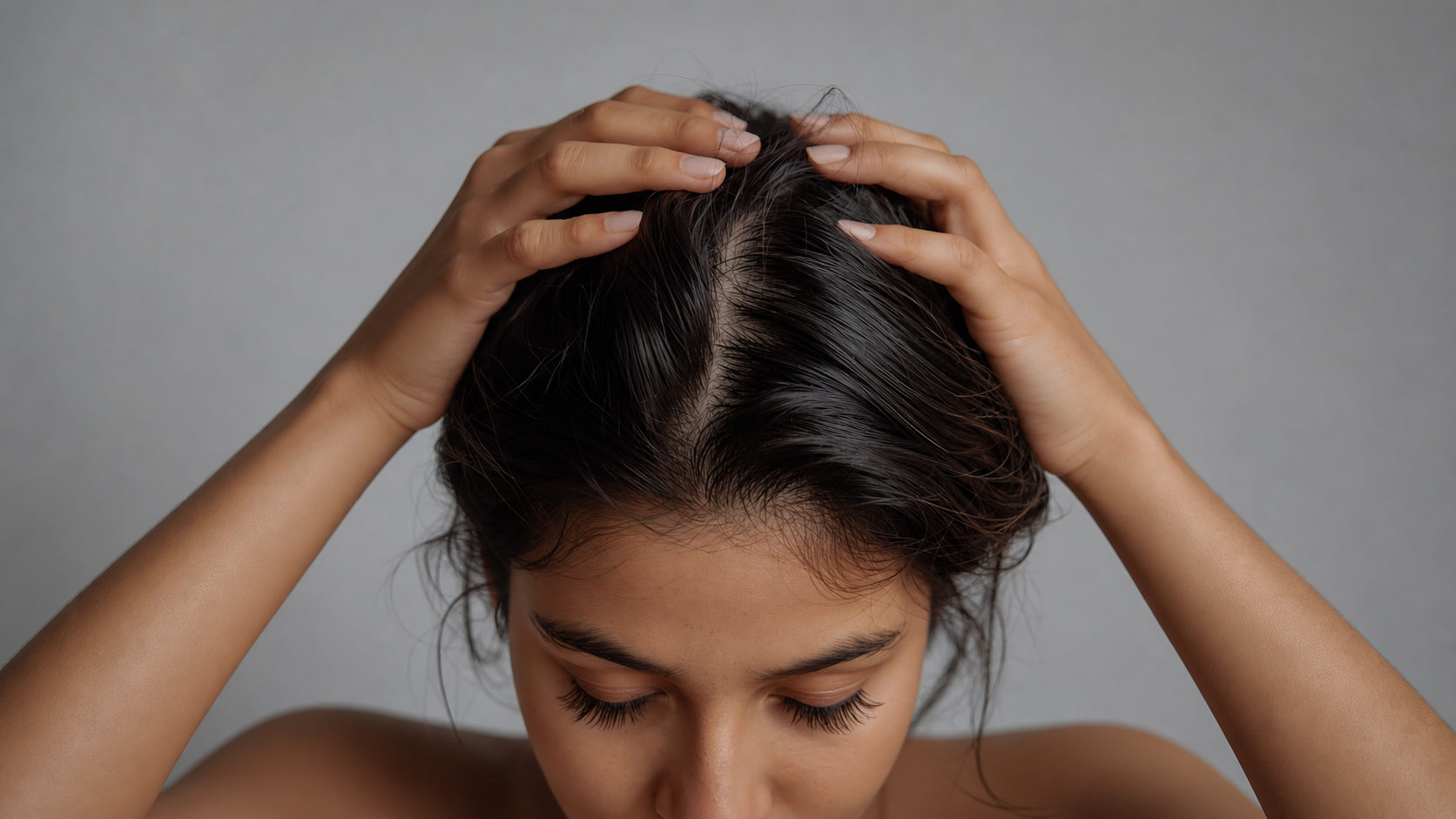 Woman gently parting dark hair with both hands to reveal a clean central scalp line.